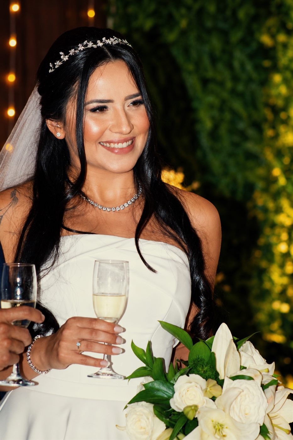 Noiva sorrindo durante o brinde, com buquê de lírios brancos