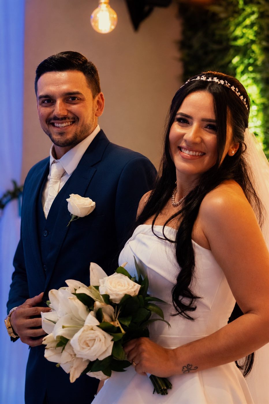 Noivos sorrindo juntos com buquê de lírios e rosas brancas