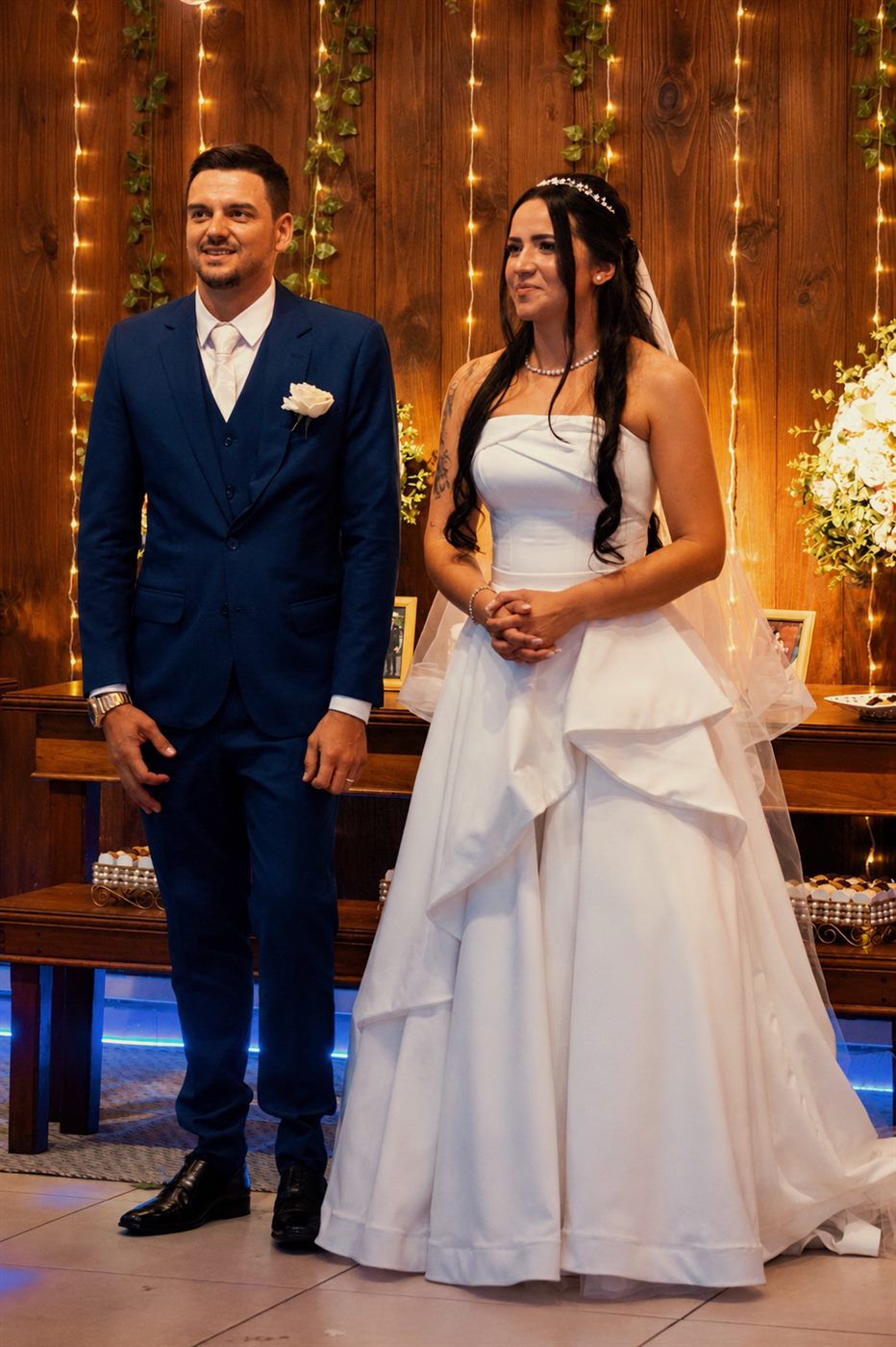 Noivos lado a lado no altar decorado com luzes e flores