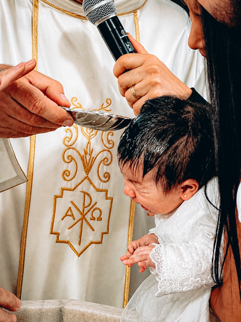 Padre derramando água benta na cabeça do bebê